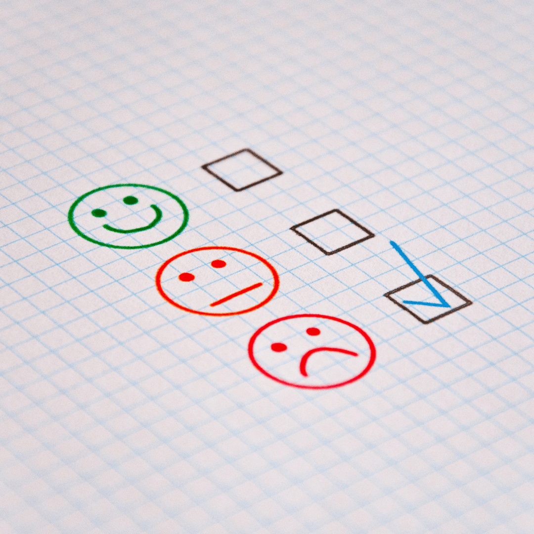 Hand-drawn smiley faces in green and red next to checkboxes represent positive, neutral, and negative satisfaction feedback on graph paper.